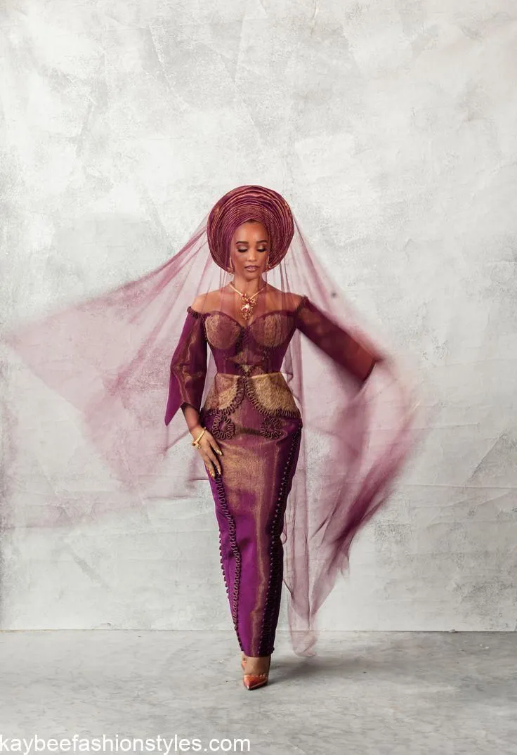 A bride in a burgundy and gold outfit with a matching gele and veil