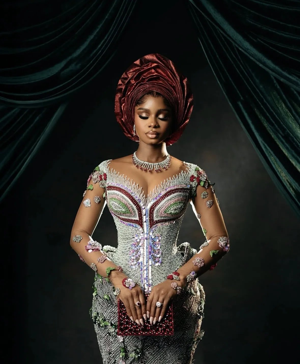 A bride in a beaded silver gown with a red gele